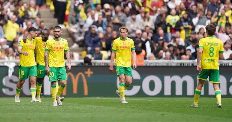 Soccer players in yellow and green kits walk on a grass field as a crowded stadium watches the match.