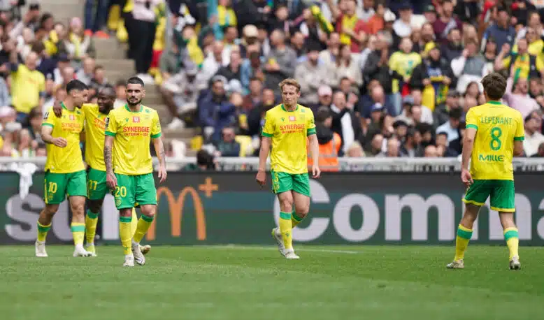 Soccer players in yellow and green kits walk on a grass field as a crowded stadium watches the match.