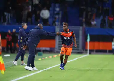 Molebe Camara | AllezPaillade.com Soccer player in orange shorts and navy jersey receives a high-five from a coach on the sideline during a match.