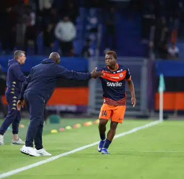 Soccer player in orange shorts and navy jersey receives a high-five from a coach on the sideline during a match.