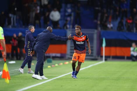 Soccer player in orange shorts and navy jersey receives a high-five from a coach on the sideline during a match.