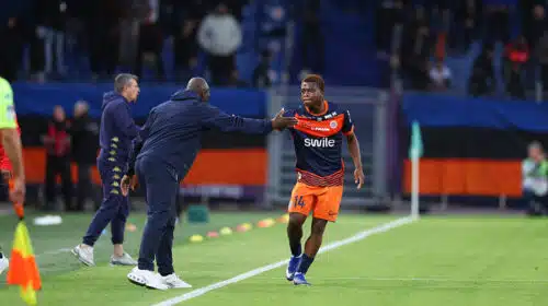 Soccer player in orange shorts and navy jersey receives a high-five from a coach on the sideline during a match.