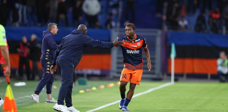 Soccer player in orange shorts and navy jersey receives a high-five from a coach on the sideline during a match.