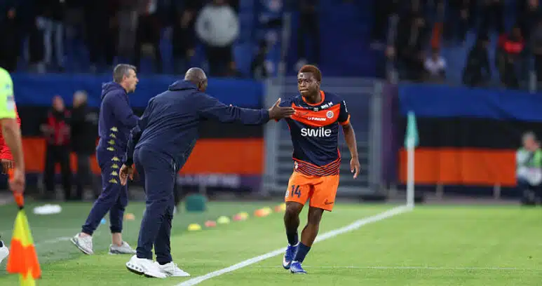 Soccer player in orange shorts and navy jersey receives a high-five from a coach on the sideline during a match.