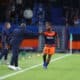Soccer player in orange shorts and navy jersey receives a high-five from a coach on the sideline during a match.