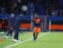 Soccer player in orange shorts and navy jersey receives a high-five from a coach on the sideline during a match.