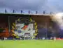 Large stadium banner reading 'Butte Paillade 34' with yellow laurel leaves behind a soccer goal; players on the pitch and orange smoke in the stands.
