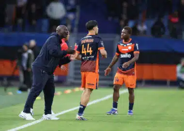 Soccer coach and players on a field during a match, one player wearing number 44 greeted by the coach at sideline before restart.