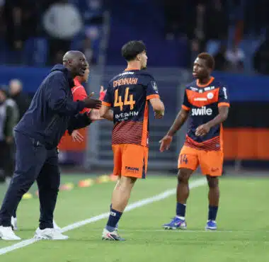 Soccer coach and players on a field during a match, one player wearing number 44 greeted by the coach at sideline before restart.