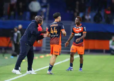 Soccer coach gesturing and talking to two players on a green field during a match.