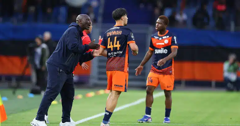 Soccer coach gesturing and talking to two players on a green field during a match.