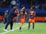 Soccer coach gesturing and talking to two players on a green field during a match.