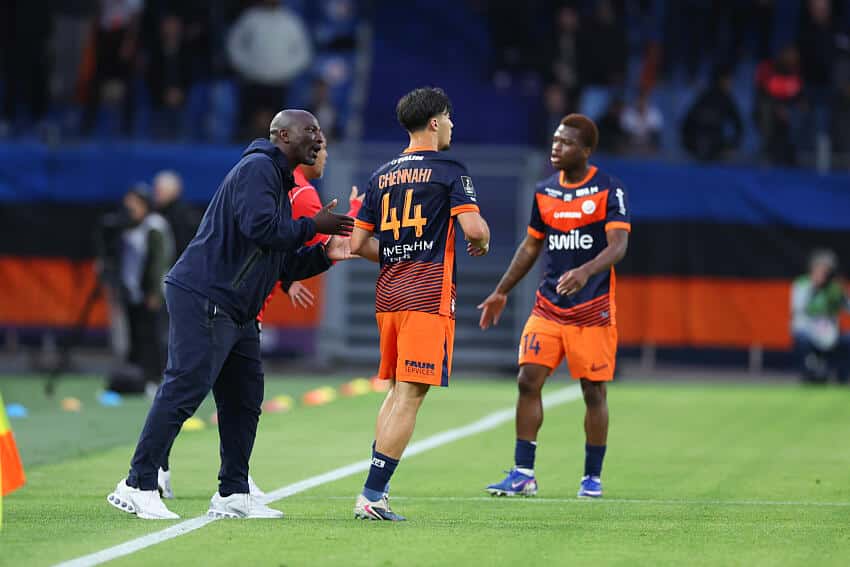 Soccer coach gesturing and talking to two players on a green field during a match.