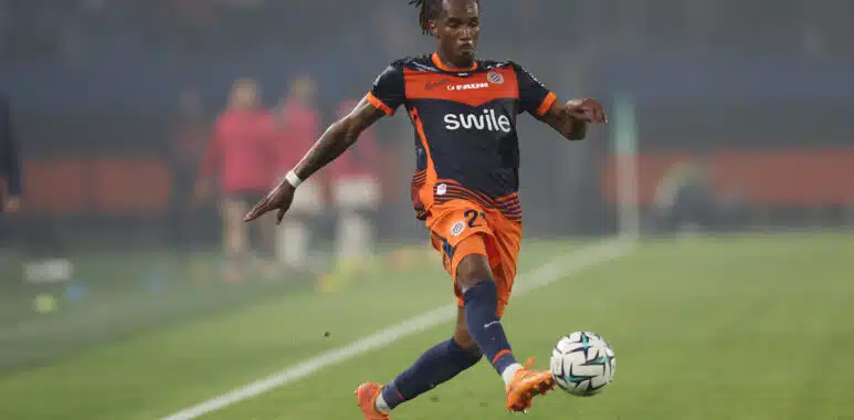 Soccer player in navy and orange kit handling a ball on a grass field during a match and focused on action to the right.