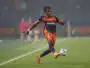 Soccer player in navy and orange kit handling a ball on a grass field during a match and focused on action to the right.