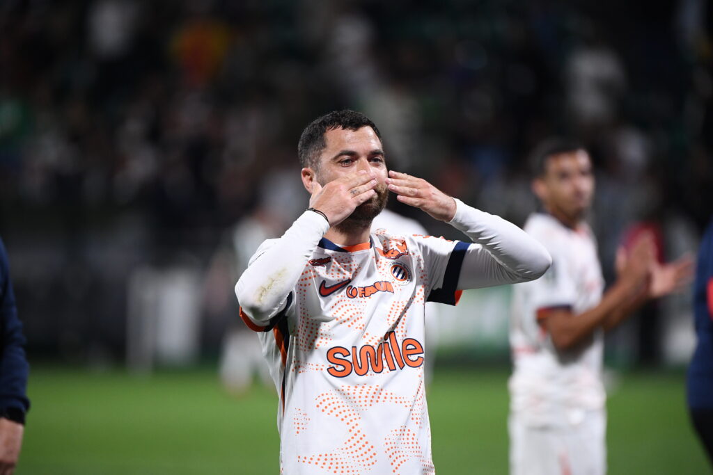 Soccer player in a white jersey celebrating, blowing a kiss with hands to lips on the field