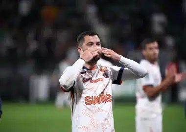 Soccer player in a white jersey celebrating, blowing a kiss with hands to lips on the field