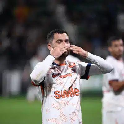 Soccer player in a white jersey celebrating, blowing a kiss with hands to lips on the field