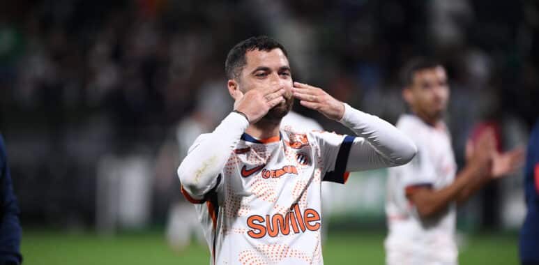 Soccer player in a white jersey celebrating, blowing a kiss with hands to lips on the field