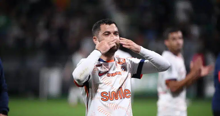 Soccer player in a white jersey celebrating, blowing a kiss with hands to lips on the field