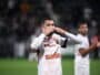 Soccer player in a white jersey celebrating, blowing a kiss with hands to lips on the field