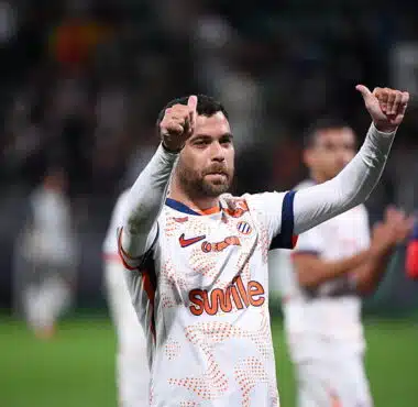 Soccer player in a white jersey with orange pattern, giving two thumbs up on the field.