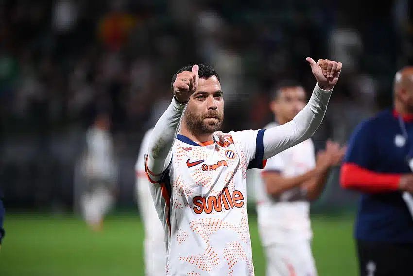 Soccer player in a white jersey with orange pattern, giving two thumbs up on the field.