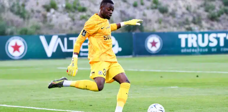 Soccer goalkeeper in a yellow kit and gloves kicking a ball on a grass field during a match.
