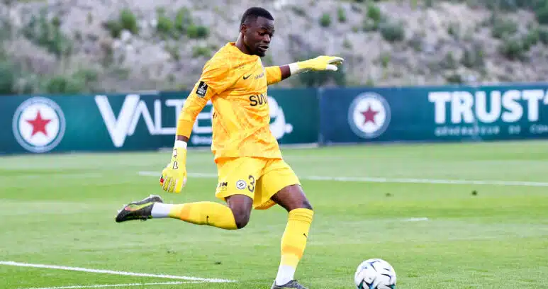Soccer goalkeeper in a yellow kit and gloves kicking a ball on a grass field during a match.