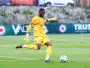 Soccer goalkeeper in a yellow kit and gloves kicking a ball on a grass field during a match.