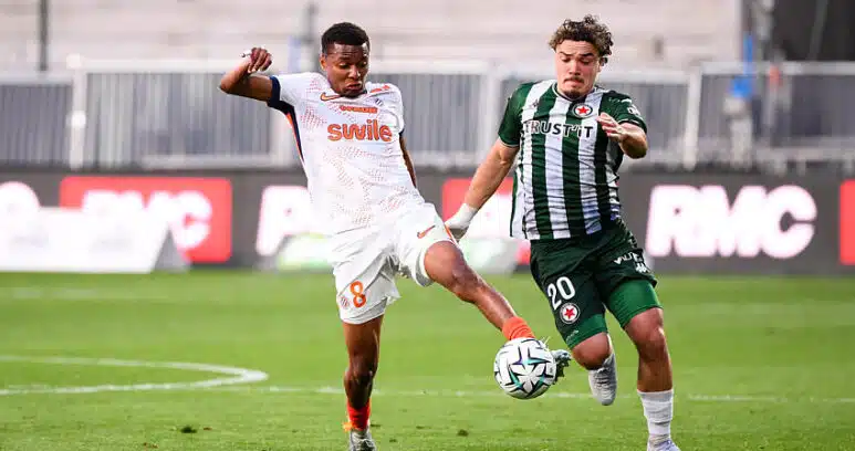 Two soccer players fight for the ball mid‑field: one in white with orange accents (number 8) and the other in green and black stripes, both challenging for possession on the grass field