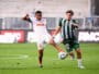 Two soccer players fight for the ball mid‑field: one in white with orange accents (number 8) and the other in green and black stripes, both challenging for possession on the grass field