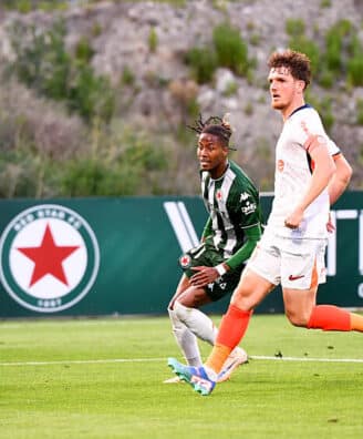 Laporte Red Star | AllezPaillade.com Two soccer players sprint after the ball on a green field, one in green-and-black stripes and the other in white with orange socks.",