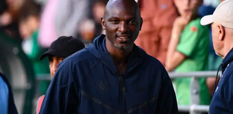 Zoumana Camara Red Star FC v Montpellier Herault SC - Ligue 2 BKT 20252026 | AllezPaillade.com Man in a navy jacket smiles as he stands at an outdoor event, with blurred crowd members in the background.