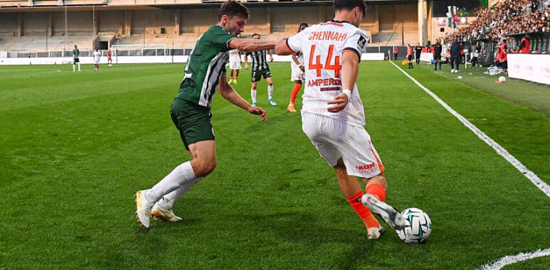 Chennahi Red Star | AllezPaillade.com Two soccer players contest the ball near the sideline on a green pitch as a white jersey #44 (Chennai) clashes with a green opponent, with stands and crowd in the background.