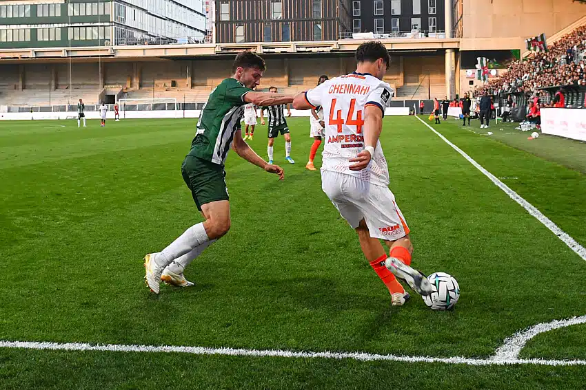 Chennahi Red Star | AllezPaillade.com Two soccer players contest the ball near the sideline on a green pitch as a white jersey #44 (Chennai) clashes with a green opponent, with stands and crowd in the background.