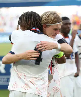 Tidiane Diallo Robin Thiland Herard Photo by Icon Sport - Photo by Icon Sport | AllezPaillade.com Two athletes in white uniforms hug in celebration on a sports field, medal visible at the neck, blurred crowd in the background.