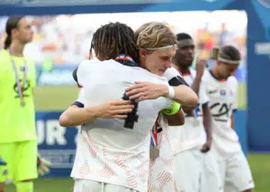 Tidiane Diallo Robin Thiland Herard Photo by Icon Sport - Photo by Icon Sport | AllezPaillade.com Two athletes in white uniforms hug in celebration on a sports field, medal visible at the neck, blurred crowd in the background.