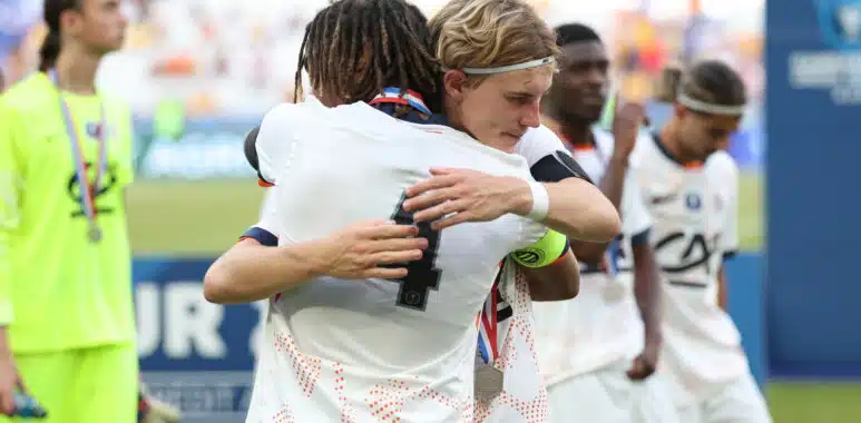Tidiane Diallo Robin Thiland Herard Photo by Icon Sport - Photo by Icon Sport | AllezPaillade.com Two athletes in white uniforms hug in celebration on a sports field, medal visible at the neck, blurred crowd in the background.