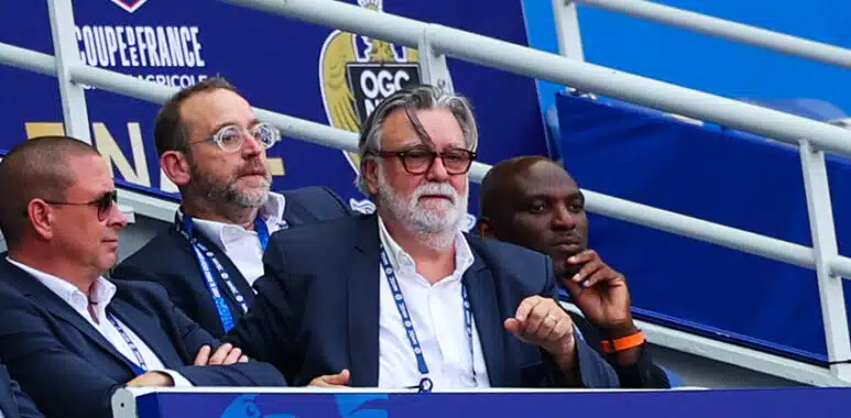 Nicollin Camara Carotti | AllezPaillade.com Group of men in suits seated in a stadium VIP box with blue banners behind them, watching the event.
