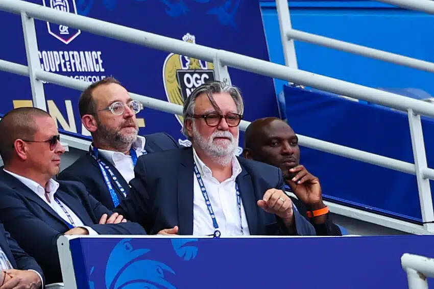 Nicollin Camara Carotti | AllezPaillade.com Group of men in suits seated in a stadium VIP box with blue banners behind them, watching the event.