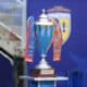 Shiny silver trophy with blue and orange ribbons on a wooden pedestal, set against a blue backdrop (awards scene).