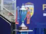 Shiny silver trophy with blue and orange ribbons on a wooden pedestal, set against a blue backdrop (awards scene).