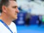 Man in a white shirt shown in profile, wearing a blue lanyard at a sports arena or venue.