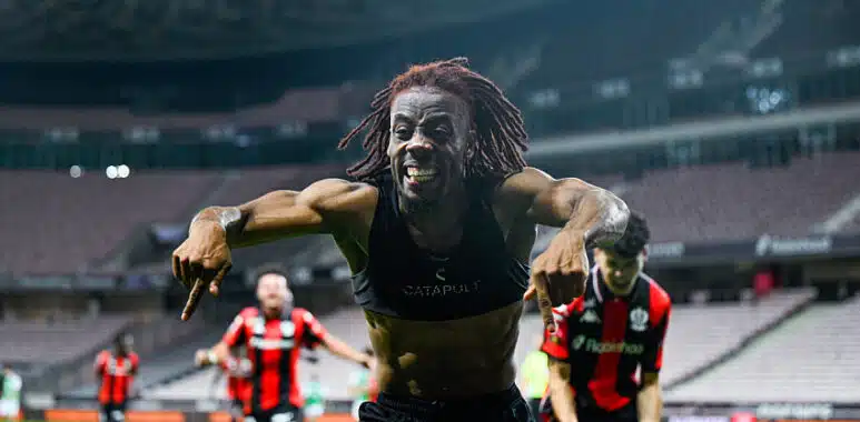 Elie Wahi | AllezPaillade.com Soccer player with dreadlocks celebrates toward the camera on a stadium field, arms outstretched and smiling.