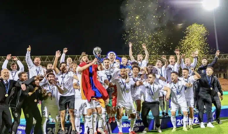 Screenshot | AllezPaillade.com Soccer team celebrates victory on a podium at night, lifting a trophy amid gold confetti.