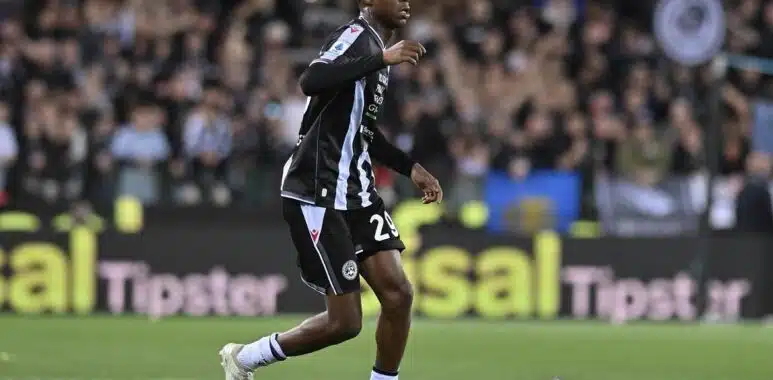 Screenshot | AllezPaillade.com Soccer player in a black and light-blue striped kit dribbles the ball on a green pitch with a cheering crowd in the background.