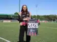 IMG_4706 | AllezPaillade.com Woman standing on a soccer field, holding a banner that reads 2028, wearing a black outfit with a red-and-black scarf.”
