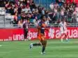 Rose Kadzere vs OL Mai 2026 Féminines | AllezPaillade.com Soccer player in orange and navy kit running on a green field during a match, with spectators in the stands behind.