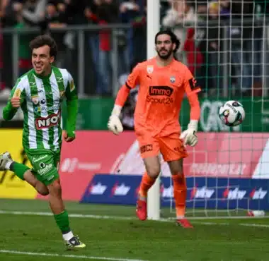Soccer scene: a green-and-white striped player celebrates near the goal as an orange-clad goalkeeper watches the ball in the air by the net.